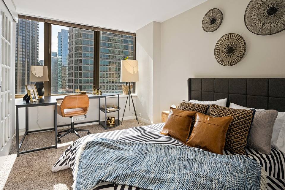 A modern bedroom with a city view, featuring a comfortable bed, stylish desk, and decorative accents.
