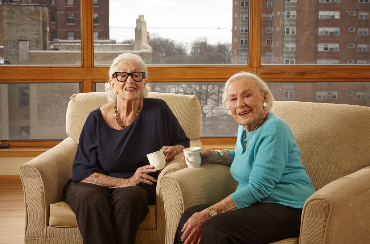 Two elderly women enjoying a conversation over tea indoors.