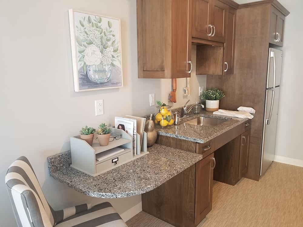 A cozy kitchen corner featuring a small workspace with a granite countertop, decorated with plants and books.