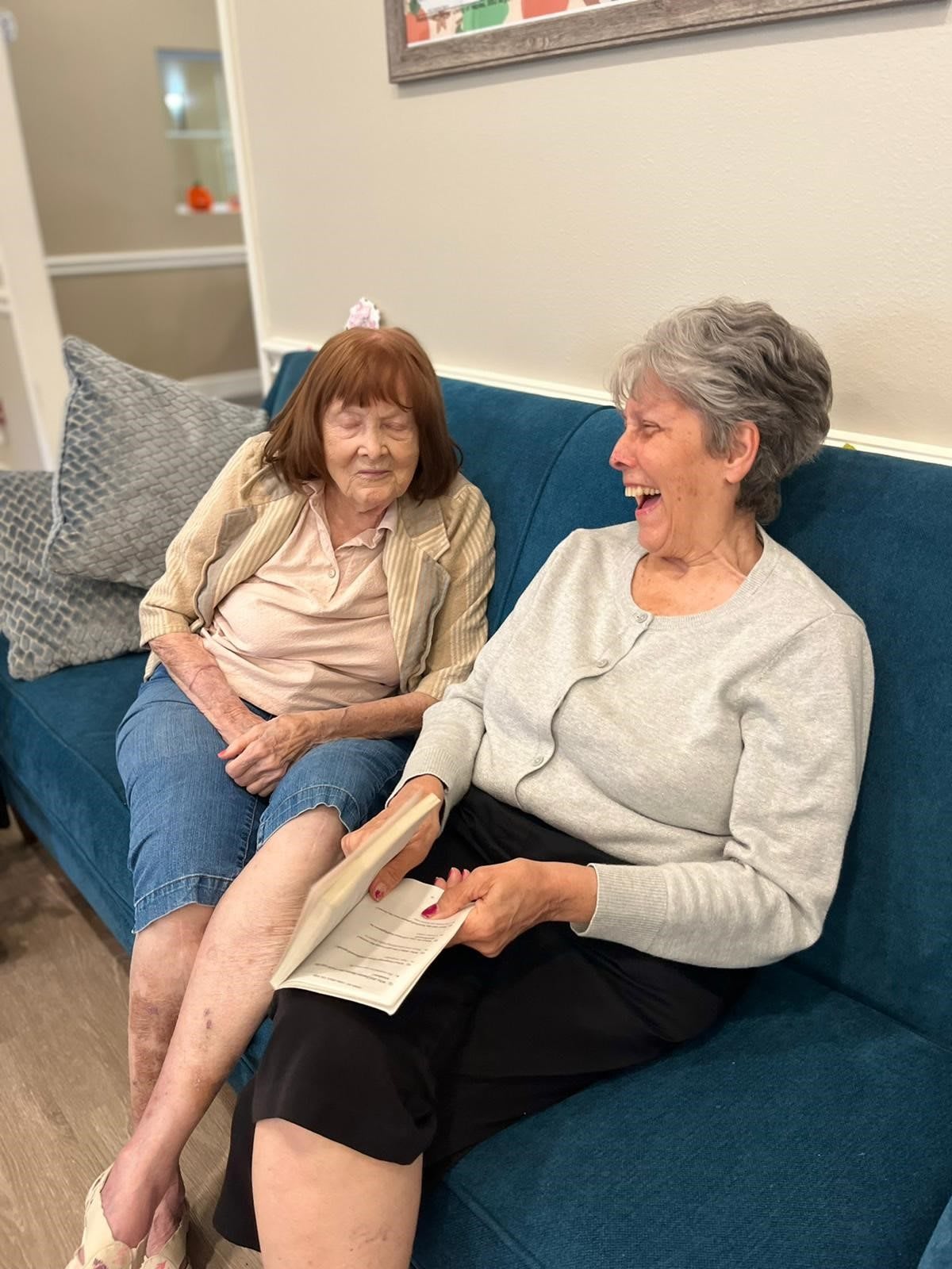Two elderly women enjoying a conversation on a couch, with one holding a book.