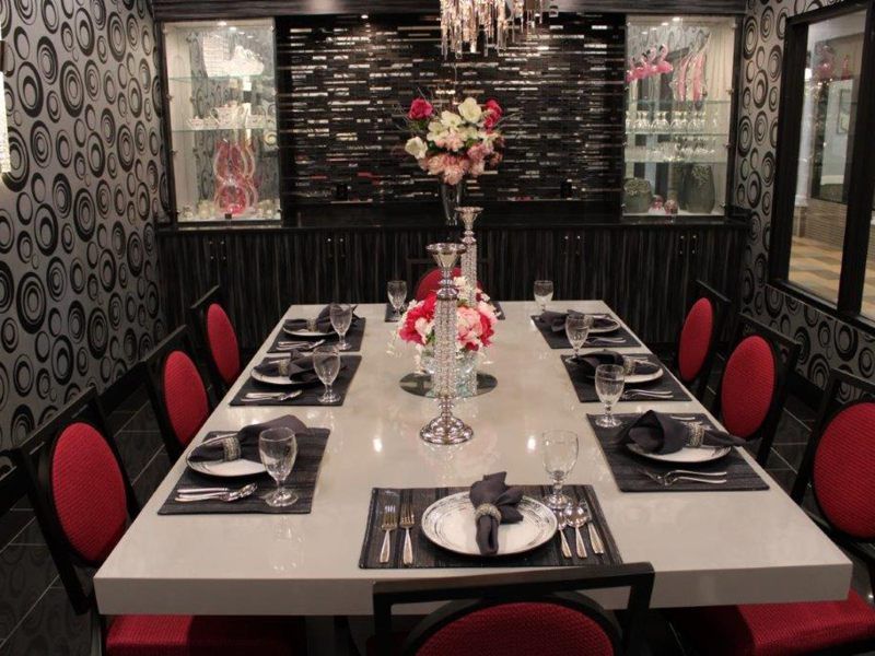 A beautifully set dining room with a modern and elegant ambiance, featuring red chairs and a floral centerpiece.