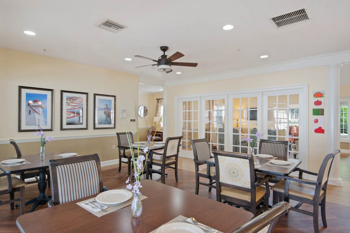A cozy dining room featuring multiple tables and chairs, decorated with framed pictures and a ceiling fan.