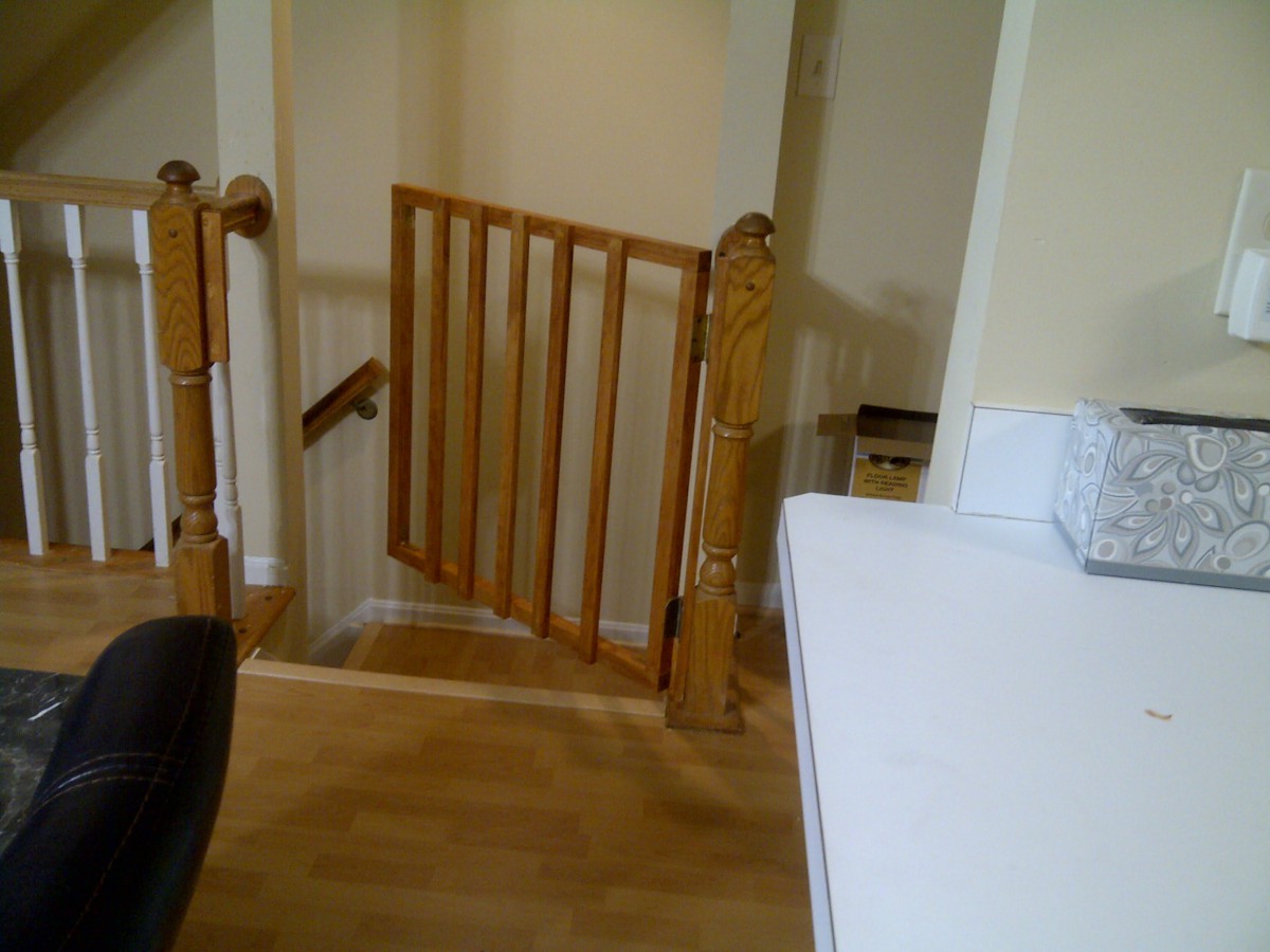 A wooden staircase with a safety gate installed at the top, leading to a lower level in a home.