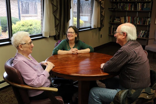 A warm gathering of three individuals engaged in conversation around a table.