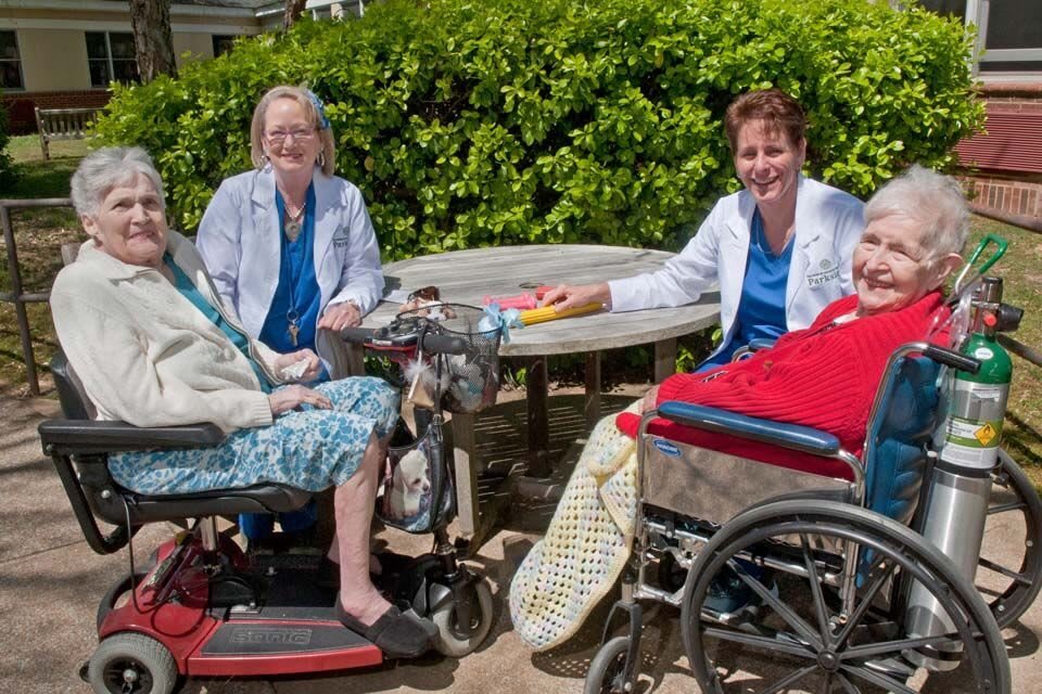 Elderly individuals with caregivers enjoying a sunny day in the garden.
