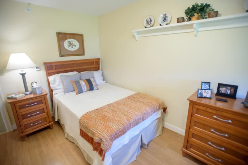 A cozy bedroom with a neatly made bed, wooden nightstands, and decorative items on a wall shelf.