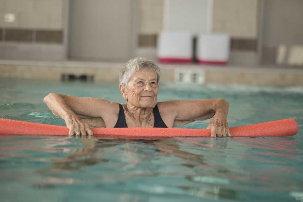 An elderly person enjoying water exercises in a swimming pool.
