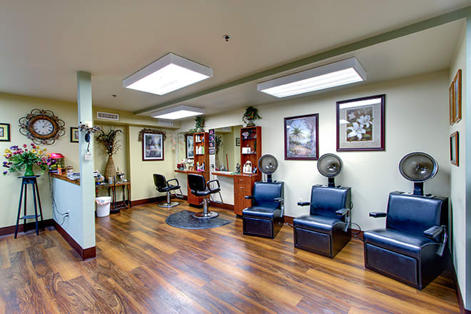 A spacious and well-organized hair salon interior with styling stations and drying chairs on a wooden floor.