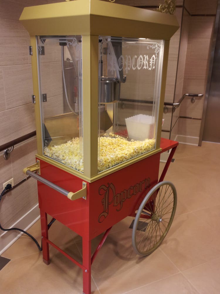 A vintage-style popcorn machine on a red cart with wheels, filled with fresh popcorn.