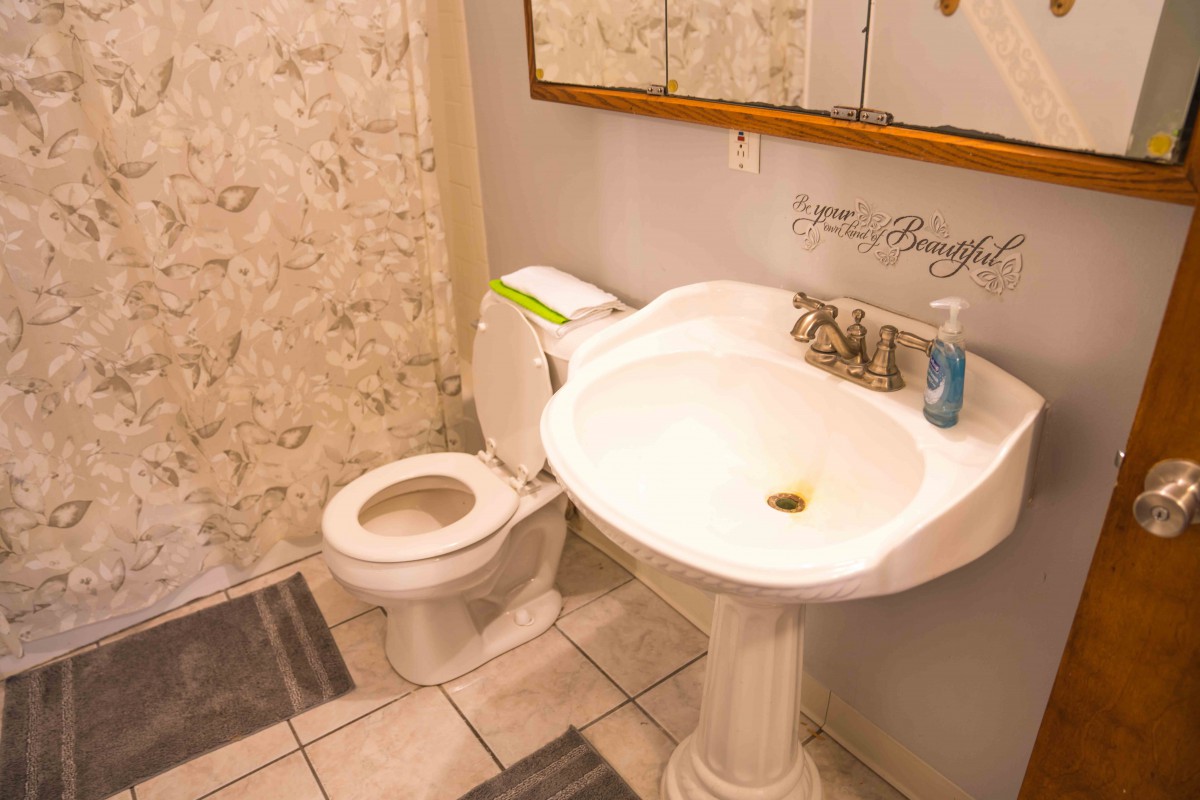 A small bathroom with a pedestal sink and toilet, featuring a tiled floor and a wall mirror.