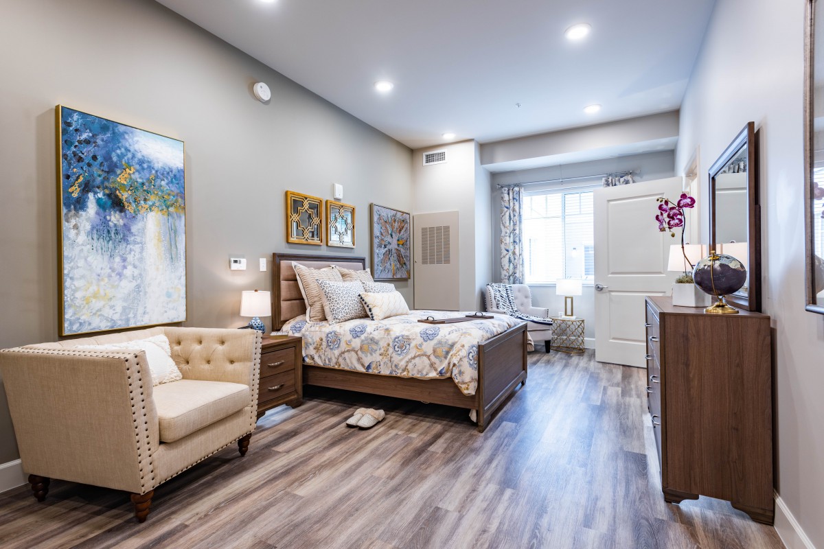 A modern and cozy bedroom featuring stylish furniture, artwork, and laminate flooring.