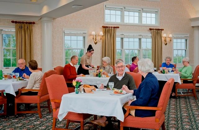 A group of seniors enjoying a meal in a restaurant setting with a waitress attending to their table.