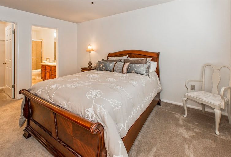 A cozy bedroom featuring a large bed with plush bedding, a lamp on a side table, and an upholstered chair.