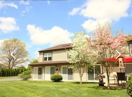 A suburban house with blooming trees and a well-kept lawn under a blue sky.