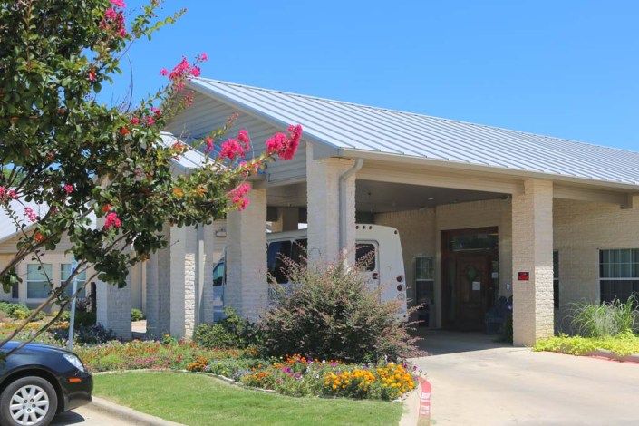 A building entrance with a covered awning and colorful landscaping.