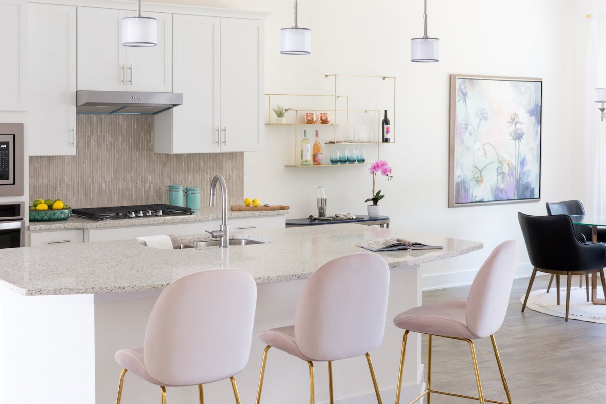 A modern kitchen featuring white cabinetry, pendant lighting, and a central island with pastel bar stools.