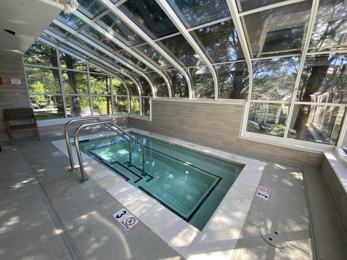 A small indoor swimming pool with a glass enclosure allowing daylight to stream in.