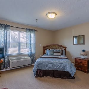 A cozy bedroom with a neatly made bed, wooden furniture, and large window with curtains.