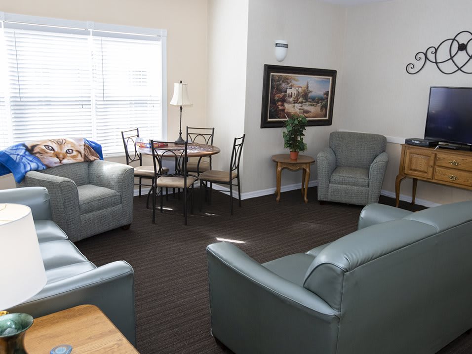 A cozy living room with armchairs, a dining table, and a painting on the wall.