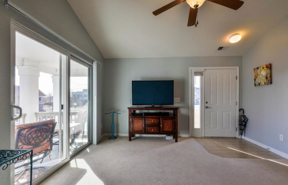 A spacious living room with a television, ceiling fan, and sliding glass door letting in natural light.