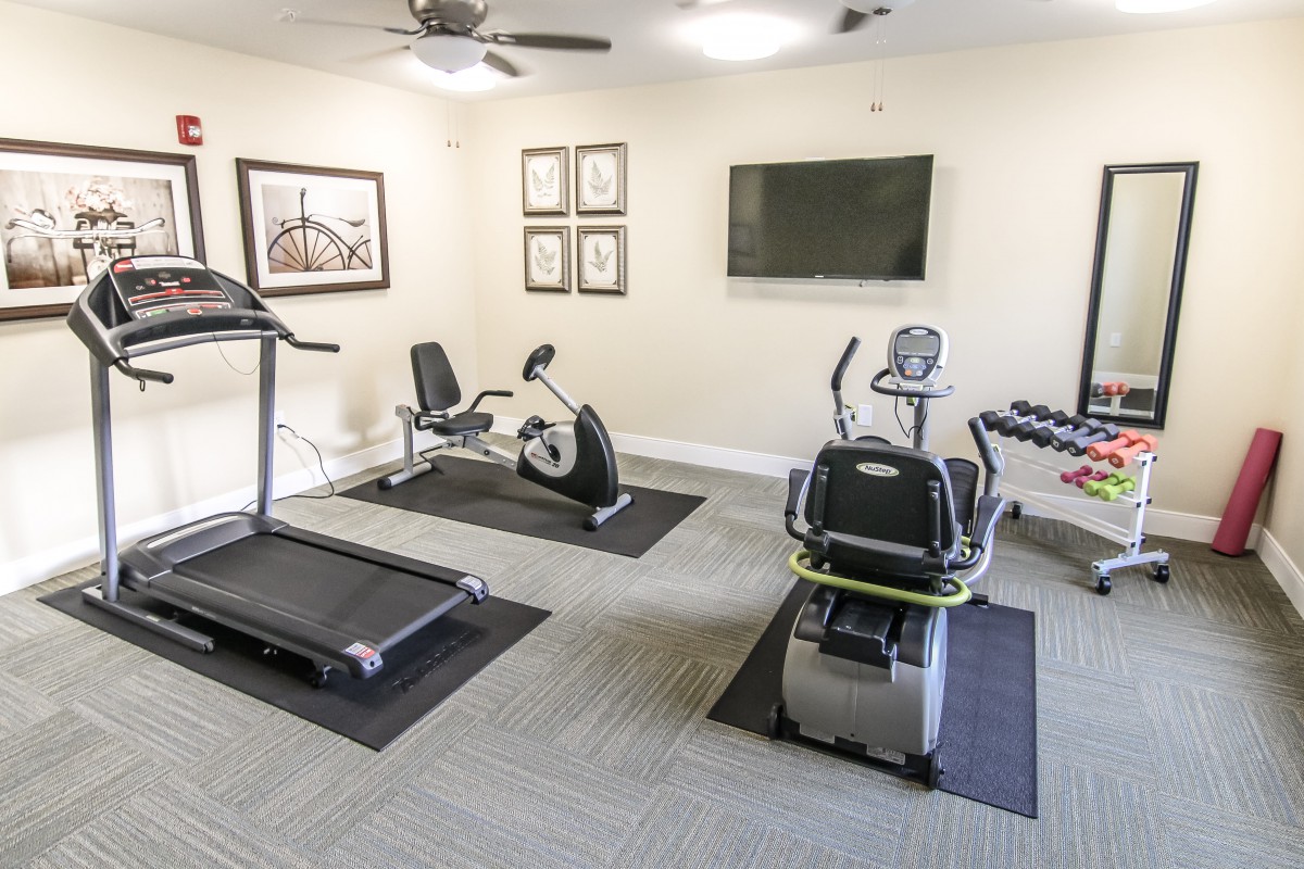 A compact fitness room equipped with a treadmill, stationary bike, and other exercise machines.