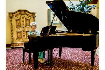 A person sitting at a grand piano in a decorated indoor setting.