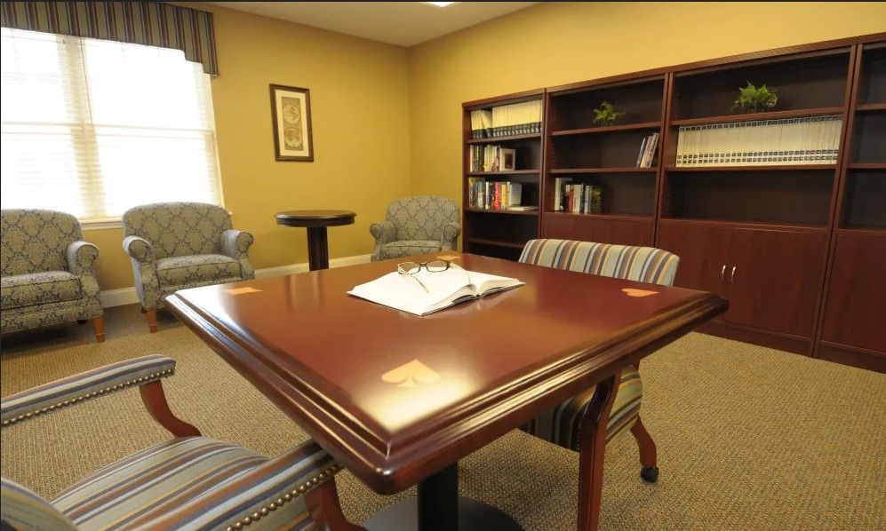 A small office meeting room with a wooden table, chairs, and a bookshelf.