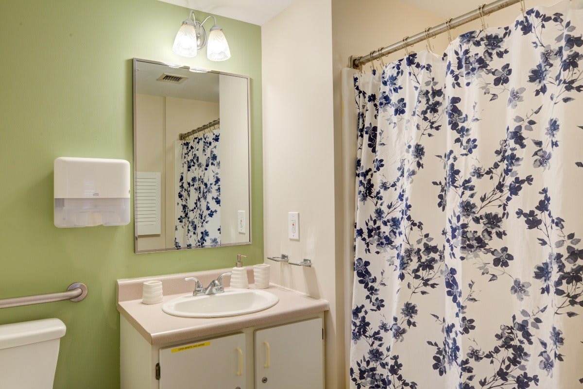 A cozy bathroom with a floral shower curtain, sink, and mirror.
