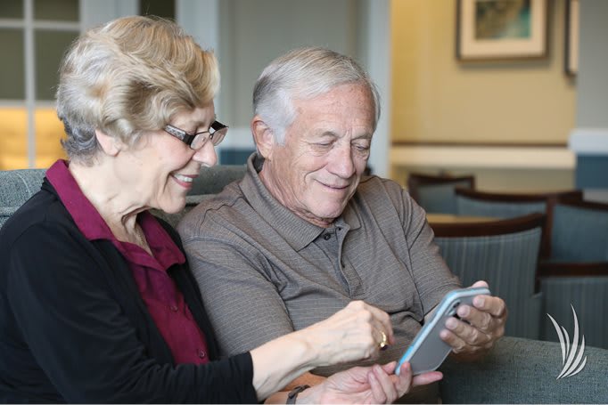 An elderly couple enjoying time together while using a tablet indoors.