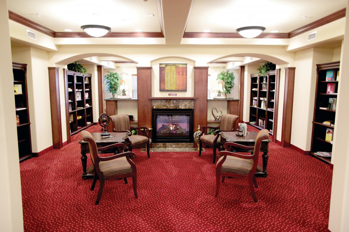 A cozy library setting with a fireplace, surrounded by bookshelves and seating arrangements.