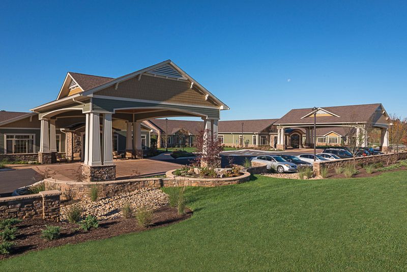 A large, modern building with a landscaped lawn and a parking lot under a clear blue sky.