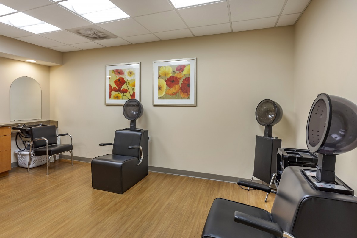 An interior view of a hair salon featuring chairs and hooded hair dryers with wall art and wooden flooring.