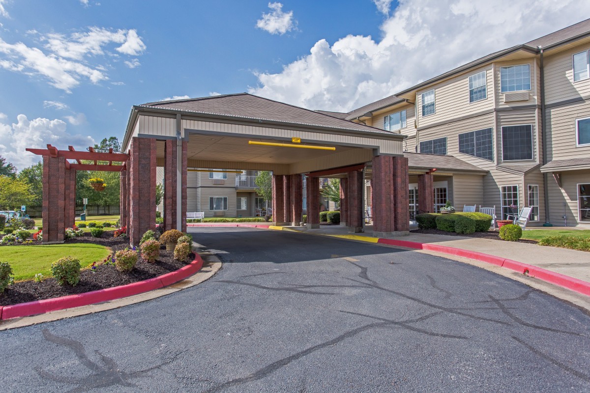 A view of a commercial building entrance with a wide driveway and well-maintained landscaping under a partly cloudy sky.