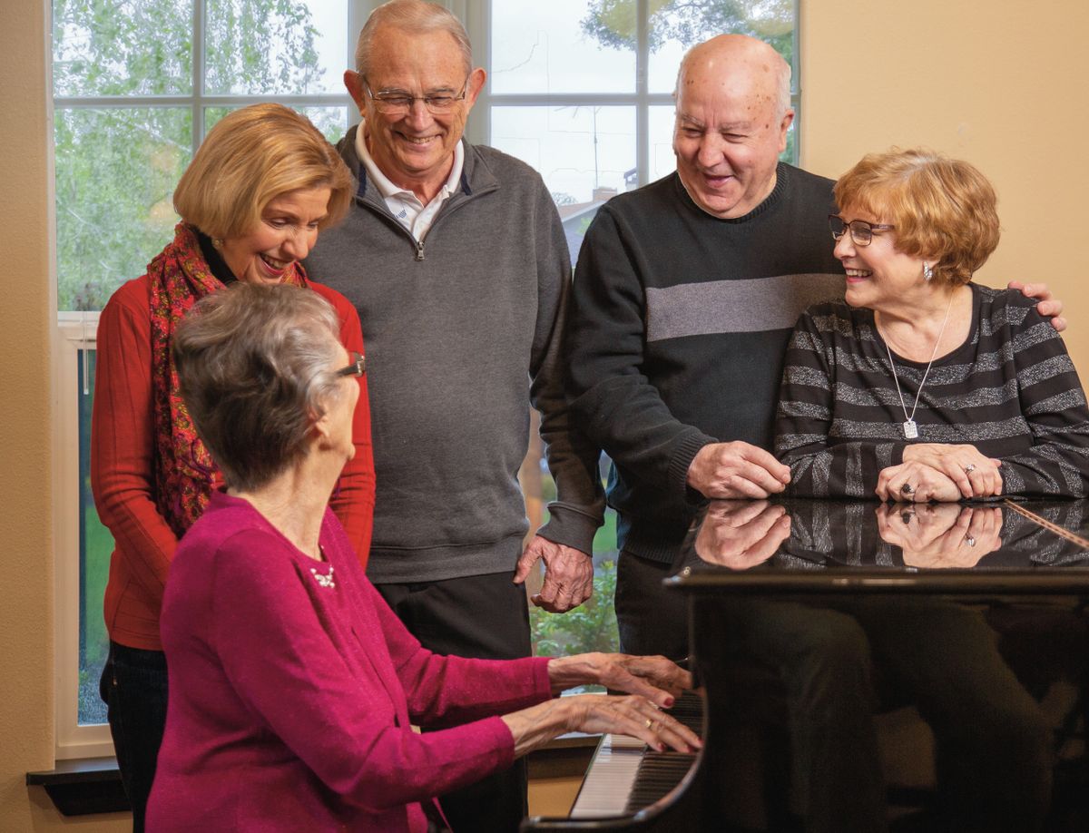 A group of seniors gathered around a piano, enjoying music and each other's company indoors.
