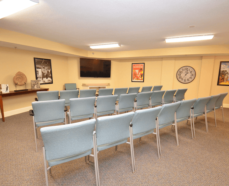 A small conference room with rows of chairs facing a television and framed pictures on the walls.