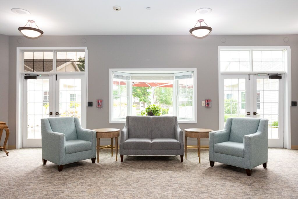 A modern living room featuring a sofa and two chairs, complemented by ample natural light through large windows.