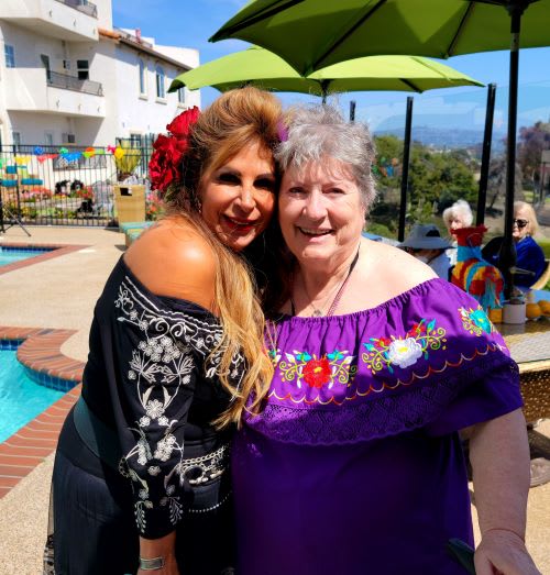 Two women in traditional clothing pose happily by a pool on a sunny day.