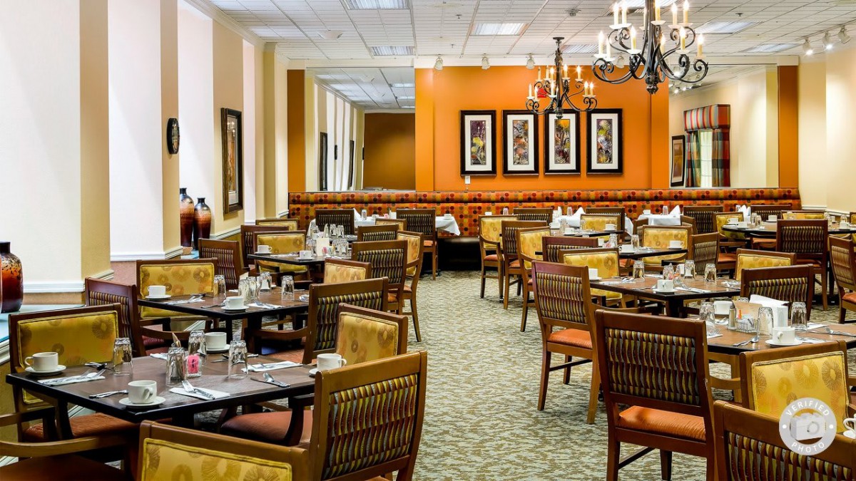 A well-decorated restaurant dining area with neatly arranged tables and chairs, featuring a warm color scheme and elegant lighting.
