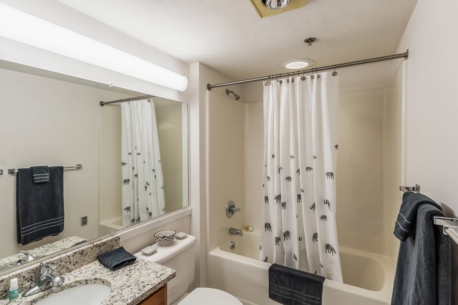 A clean and well-lit bathroom with a bathtub, shower curtain, sink, and toilet.
