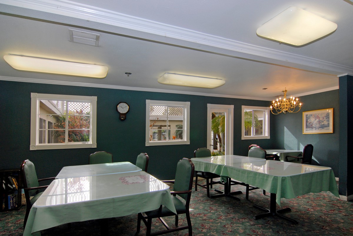 A dining room with multiple tables and chairs, featuring large windows and a chandelier.