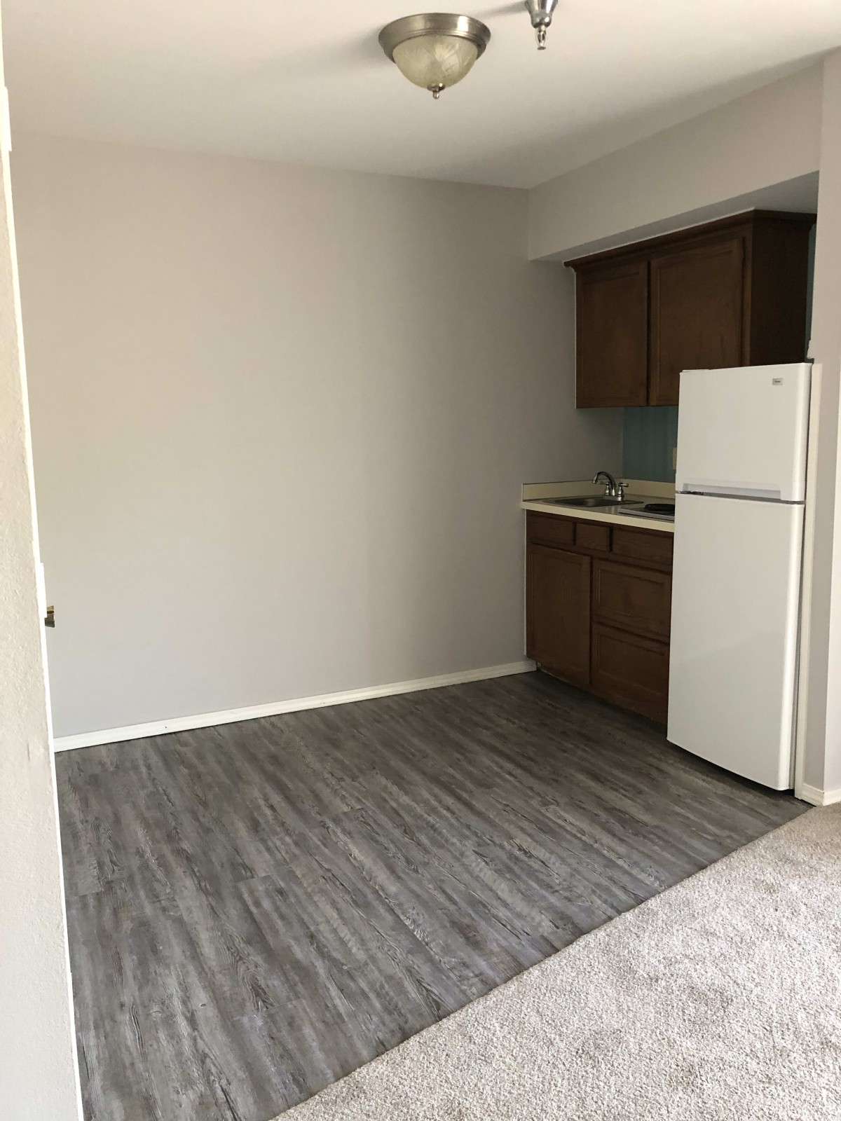 Empty kitchen space in an apartment with wooden cabinets and a gray floor.