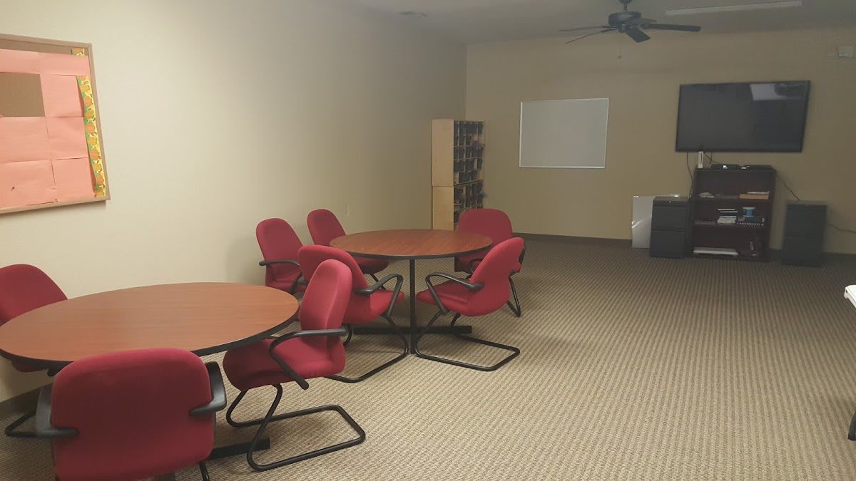 A meeting room with red chairs, round tables, and a projector screen.