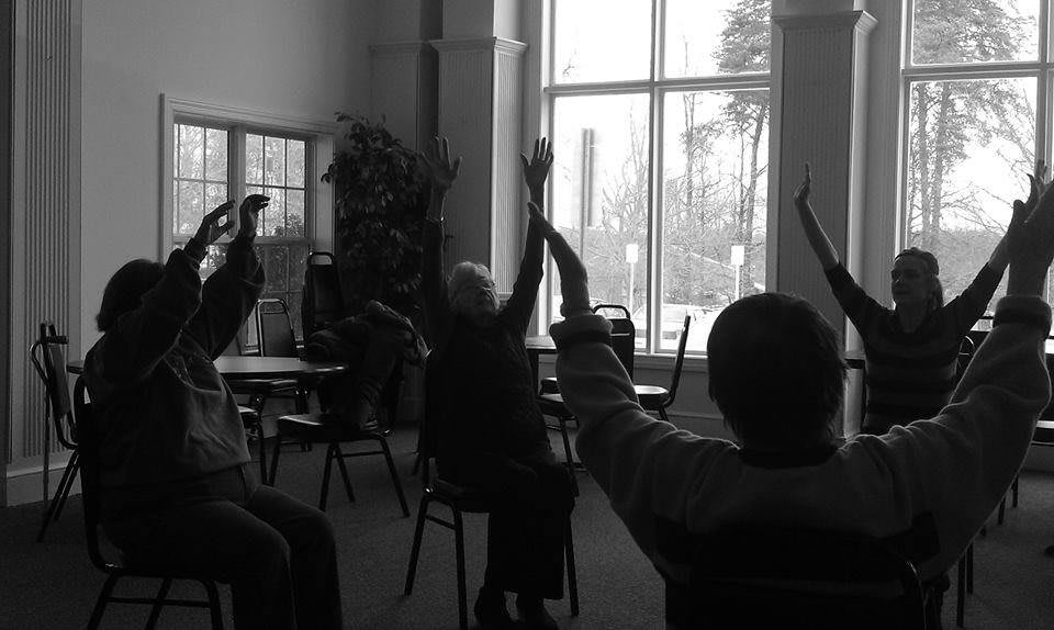 A group of seniors participating in a seated exercise session indoors.