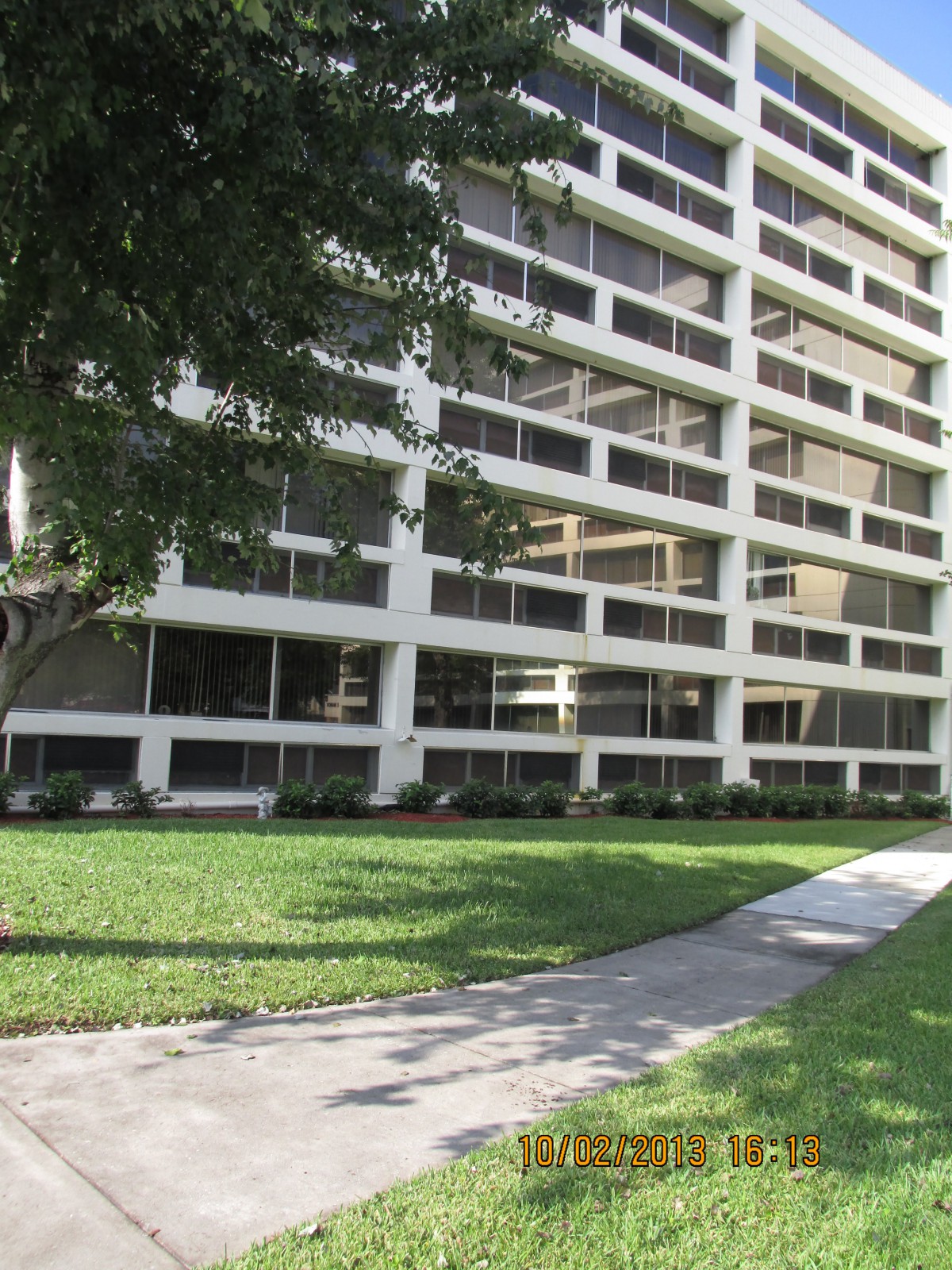 A high-rise building with large windows surrounded by a grassy area and sidewalk.
