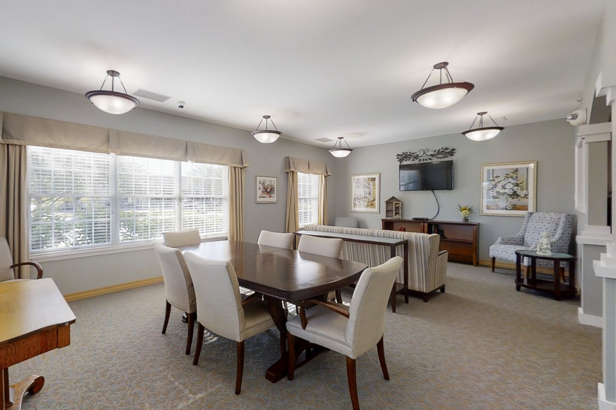 A modern dining or conference room with a large table, chairs, and a wall-mounted television.
