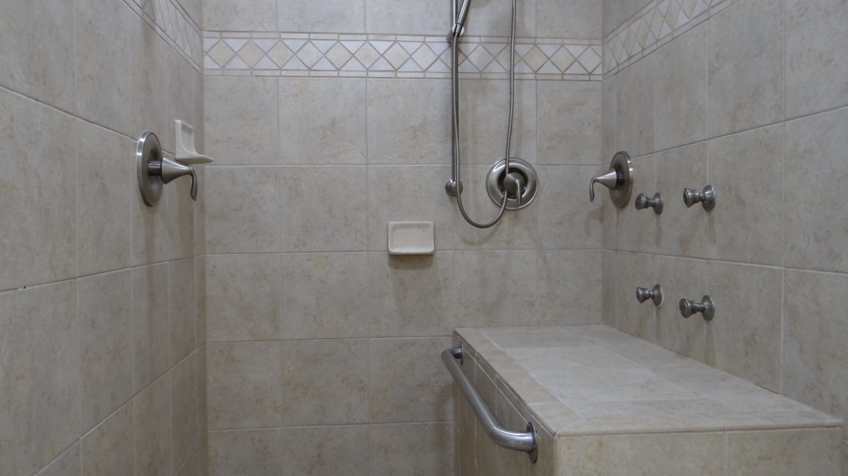 A tiled shower with a built-in bench and handrail.