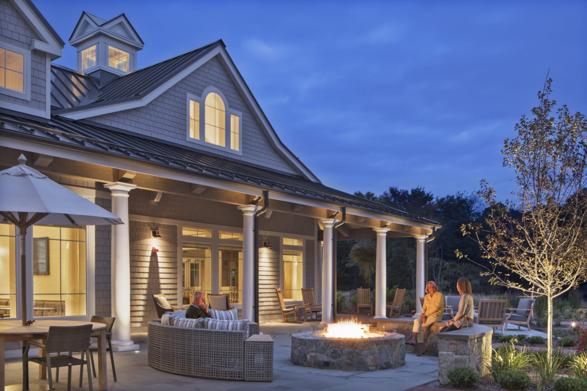 A cozy house with a lit fire pit on the porch during the evening.