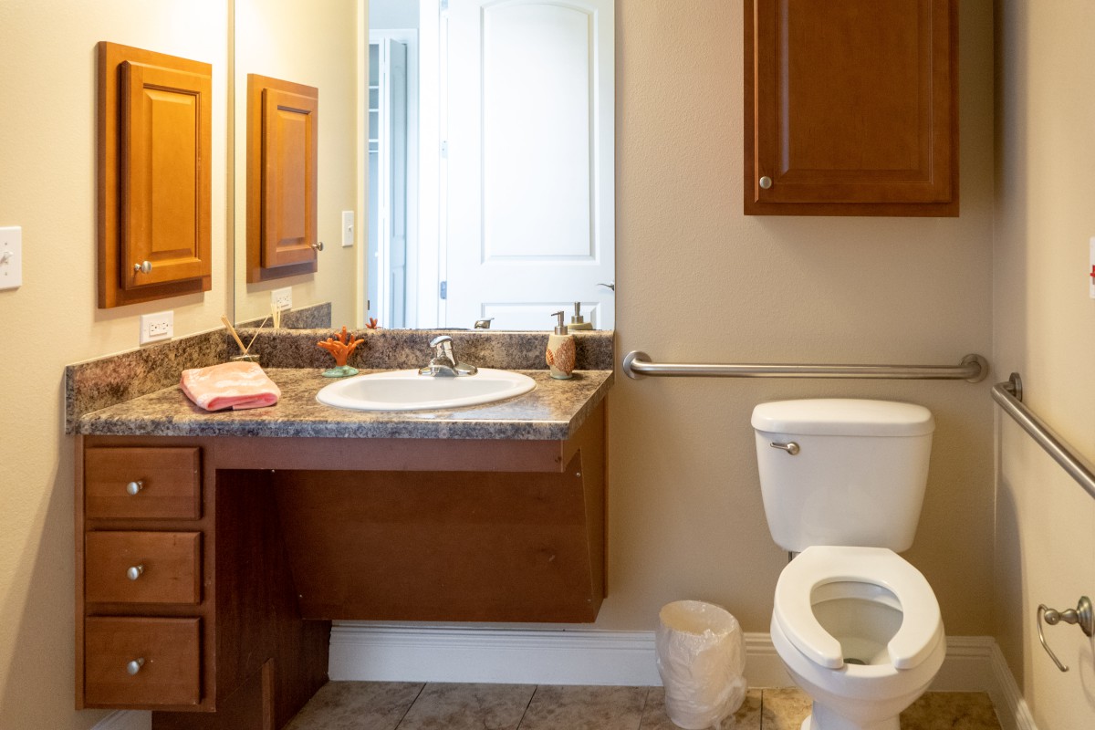 A clean and organized bathroom with a wall-mounted sink, countertop, toilet, and mirror.