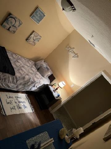 A cozy bedroom featuring a neatly made bed, wall art, and a bedside lamp.