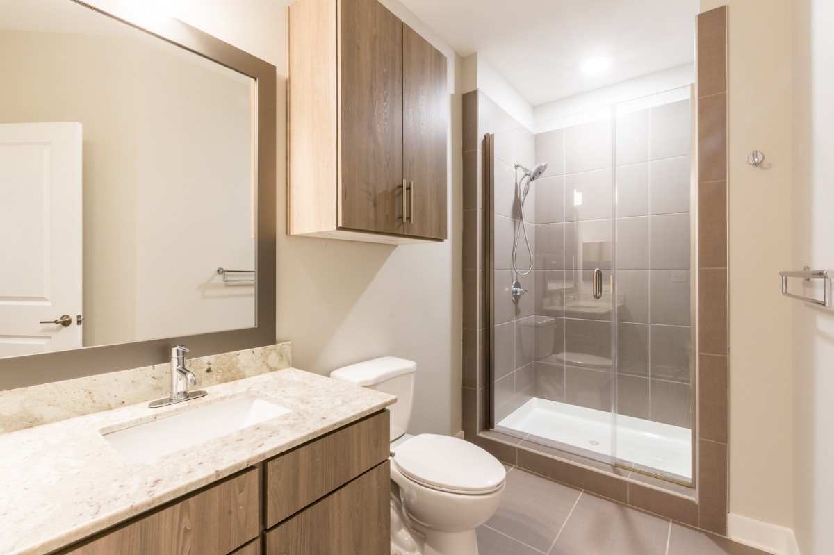 A modern bathroom with a glass-door shower, wooden cabinetry, and a marble-top vanity.